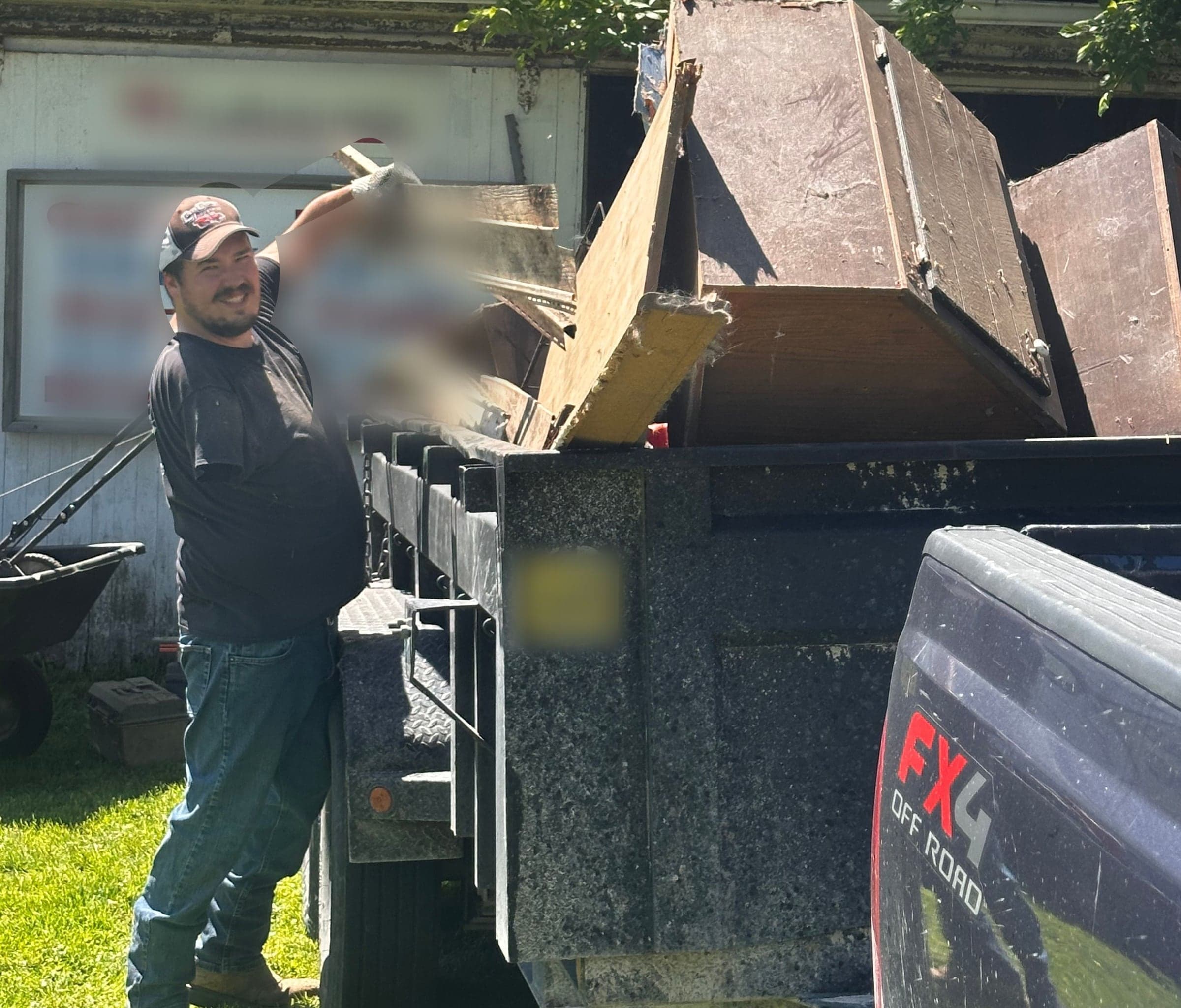 Cole lifting a board into the dump trailer with a couch already loaded, one-handed
