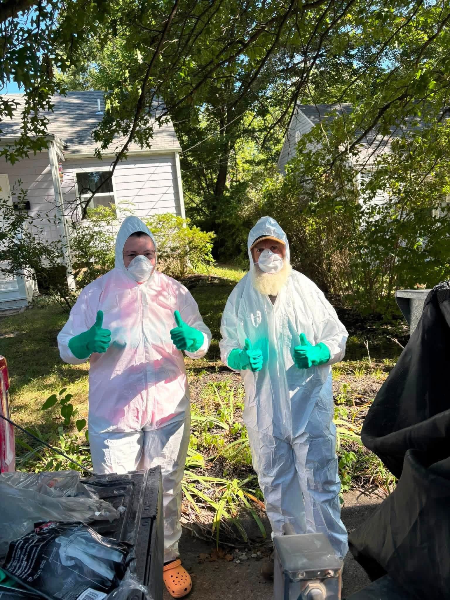 The two-person Missouri Junkers crew in protective suits giving thumbs up at a property cleanout
