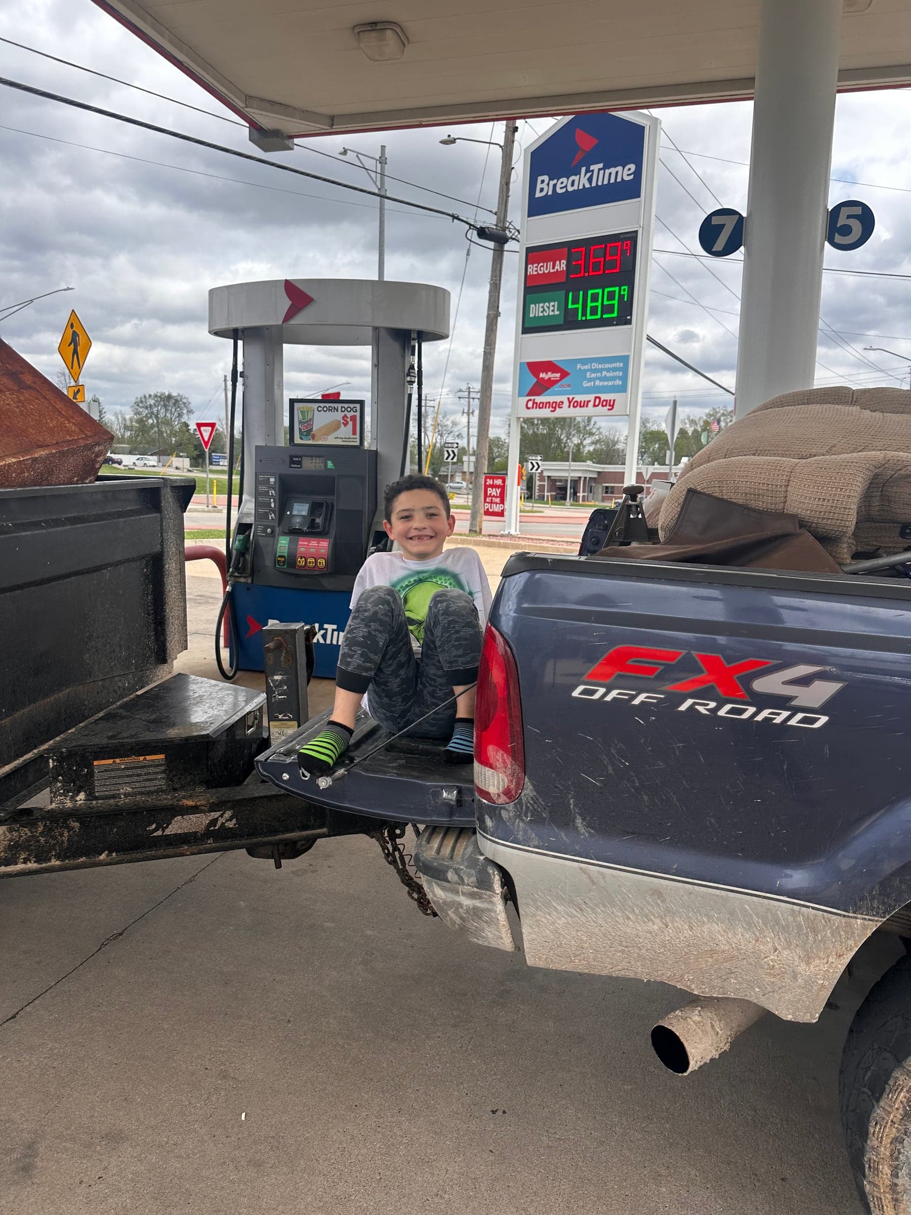 A child sitting on the truck tailgate at a gas station with the trailer loaded behind