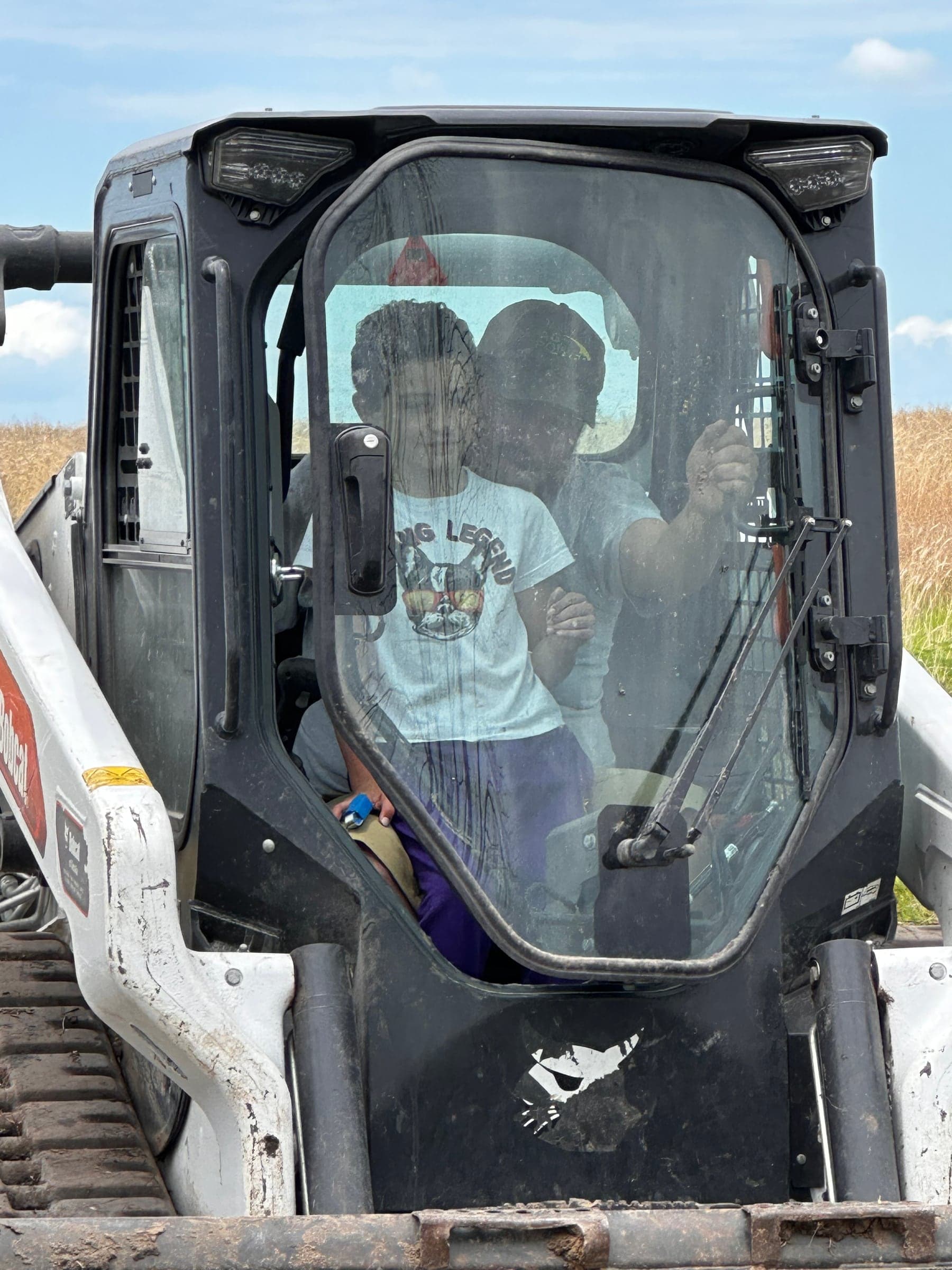 Two children smiling from inside the cab of a skid steer