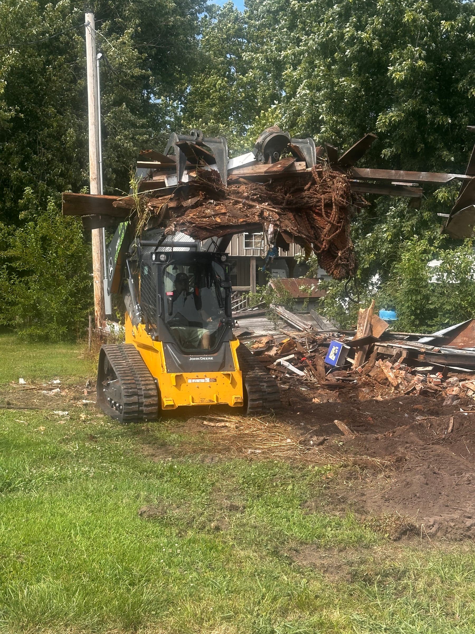 A skid steer lifting torn-down structure debris in its bucket