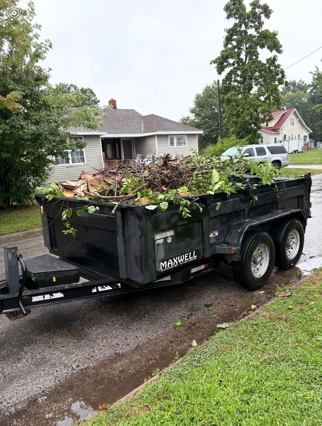 A dump trailer full of tree limbs and leaves on a residential street